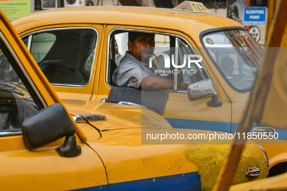 A taxi driver sits inside his yellow taxi, waiting for customers near Sealdah railway station in Kolkata, India. 