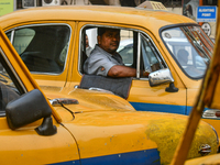 A taxi driver sits inside his yellow taxi, waiting for customers near Sealdah railway station in Kolkata, India. (