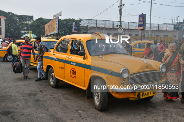 Passengers walk past a yellow taxi near Sealdah railway station in Kolkata. 