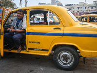 A taxi driver sits inside his yellow taxi, waiting for customers near Sealdah railway station in Kolkata, India. (