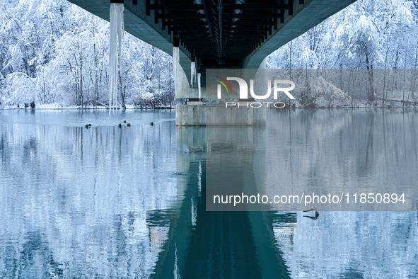 In Füssen, Bavaria, Germany, on January 13, 2024, the River Lech flows gently beneath a frosted bridge, reflecting the snowy Allgäu Alps. Th...