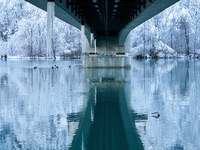 In Füssen, Bavaria, Germany, on January 13, 2024, the River Lech flows gently beneath a frosted bridge, reflecting the snowy Allgäu Alps. Th...