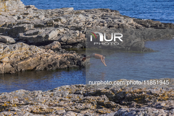 A man jumps into the Baltic Sea waters from the rocky coast in Gudhjem, Bornholm Island, Denmark, on August 6, 2024. 