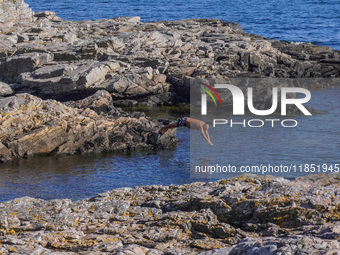 A man jumps into the Baltic Sea waters from the rocky coast in Gudhjem, Bornholm Island, Denmark, on August 6, 2024. (