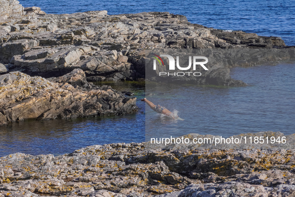 A man jumps into the Baltic Sea waters from the rocky coast in Gudhjem, Bornholm Island, Denmark, on August 6, 2024. 