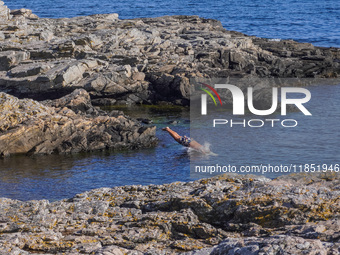 A man jumps into the Baltic Sea waters from the rocky coast in Gudhjem, Bornholm Island, Denmark, on August 6, 2024. (