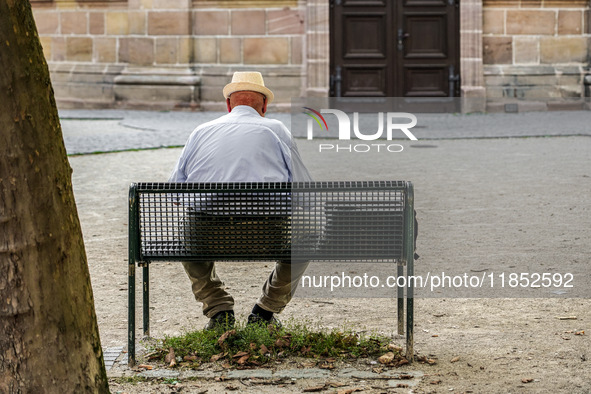 An elderly man sits quietly on a bench in a shaded courtyard in Erlangen, Germany, on September 8, 2023, his straw hat shielding him from th...