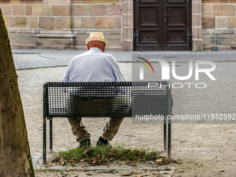 An elderly man sits quietly on a bench in a shaded courtyard in Erlangen, Germany, on September 8, 2023, his straw hat shielding him from th...