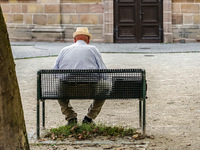 An elderly man sits quietly on a bench in a shaded courtyard in Erlangen, Germany, on September 8, 2023, his straw hat shielding him from th...