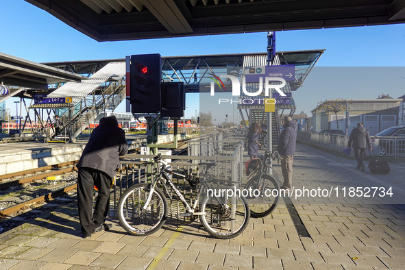 At Mühldorf station in Bavaria, Germany, on November 30, 2024, a small group of travelers waits patiently on the platform. The scene is calm...