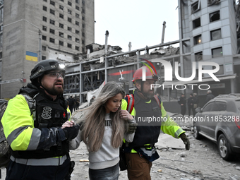 In Zaporizhzhia, Ukraine, on December 10, 2024, first responders support a woman as they walk past a building destroyed by a Russian missile...