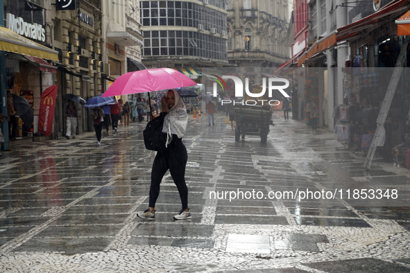 People walk with their umbrellas on a cloudy and rainy day in the center of Sao Paulo, Brazil, on December 10, 2024. 