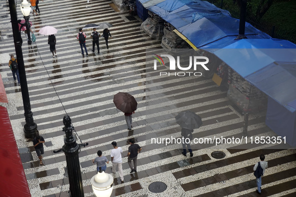 People walk with their umbrellas on a cloudy and rainy day in the center of Sao Paulo, Brazil, on December 10, 2024. 