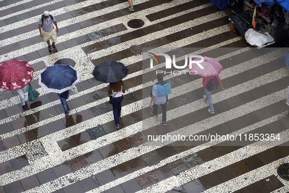 People walk with their umbrellas on a cloudy and rainy day in the center of Sao Paulo, Brazil, on December 10, 2024. 