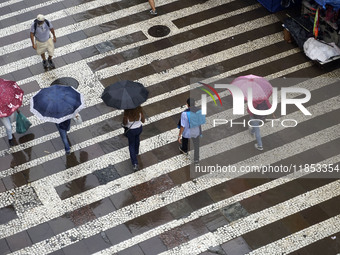 People walk with their umbrellas on a cloudy and rainy day in the center of Sao Paulo, Brazil, on December 10, 2024. (