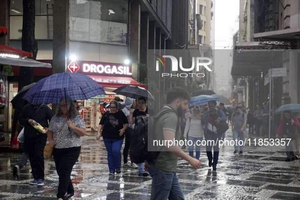 People walk with their umbrellas on a cloudy and rainy day in the center of Sao Paulo, Brazil, on December 10, 2024. 