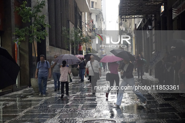 People walk with their umbrellas on a cloudy and rainy day in the center of Sao Paulo, Brazil, on December 10, 2024. 