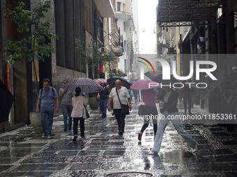 People walk with their umbrellas on a cloudy and rainy day in the center of Sao Paulo, Brazil, on December 10, 2024. (