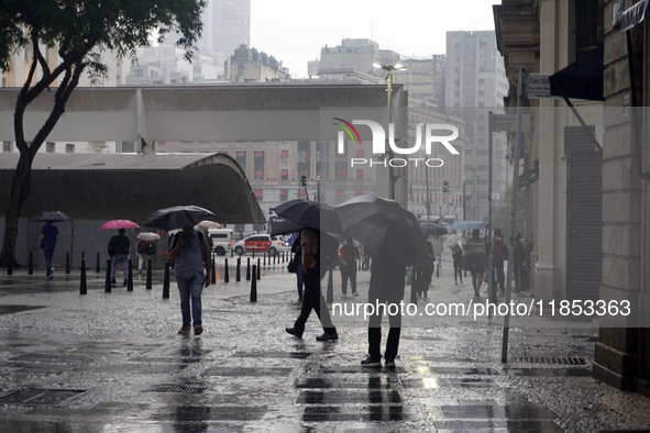 People walk with their umbrellas on a cloudy and rainy day in the center of Sao Paulo, Brazil, on December 10, 2024. 