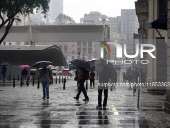 People walk with their umbrellas on a cloudy and rainy day in the center of Sao Paulo, Brazil, on December 10, 2024. (