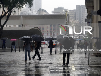 People walk with their umbrellas on a cloudy and rainy day in the center of Sao Paulo, Brazil, on December 10, 2024. (