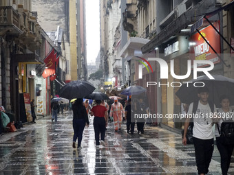 People walk with their umbrellas on a cloudy and rainy day in the center of Sao Paulo, Brazil, on December 10, 2024. (