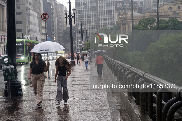 People walk with their umbrellas on a cloudy and rainy day in the center of Sao Paulo, Brazil, on December 10, 2024. 