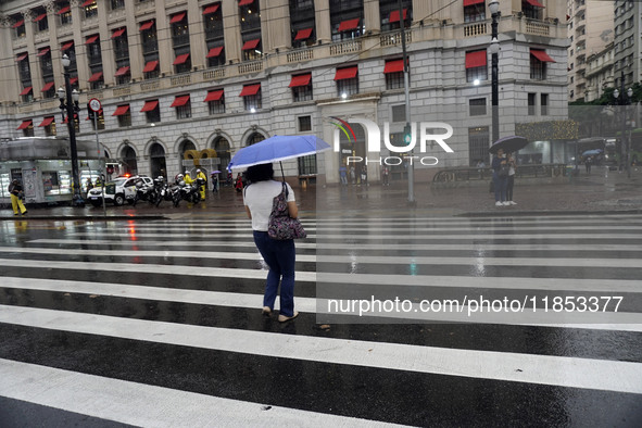 People walk with their umbrellas on a cloudy and rainy day in the center of Sao Paulo, Brazil, on December 10, 2024. 