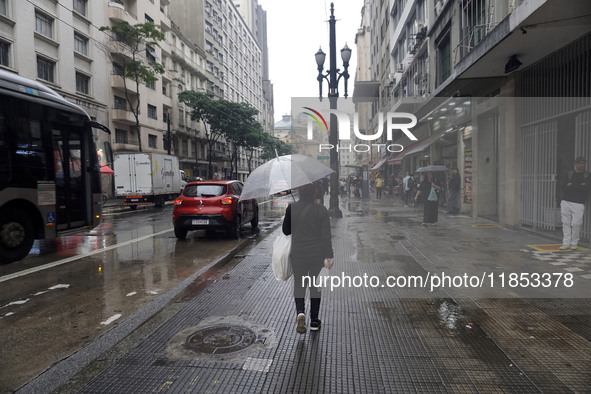 People walk with their umbrellas on a cloudy and rainy day in the center of Sao Paulo, Brazil, on December 10, 2024. 