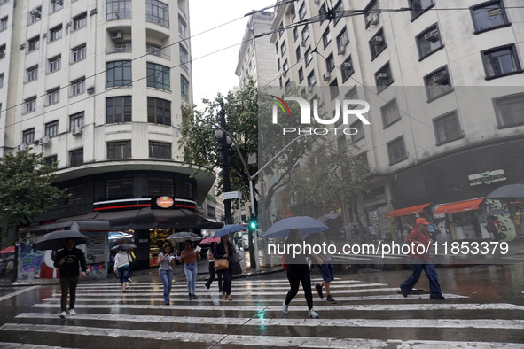 People walk with their umbrellas on a cloudy and rainy day in the center of Sao Paulo, Brazil, on December 10, 2024. 