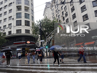 People walk with their umbrellas on a cloudy and rainy day in the center of Sao Paulo, Brazil, on December 10, 2024. (