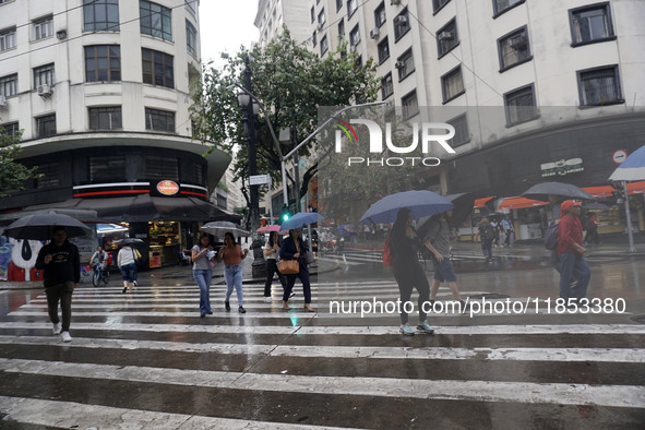 People walk with their umbrellas on a cloudy and rainy day in the center of Sao Paulo, Brazil, on December 10, 2024. 