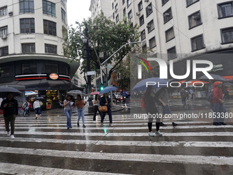 People walk with their umbrellas on a cloudy and rainy day in the center of Sao Paulo, Brazil, on December 10, 2024. (