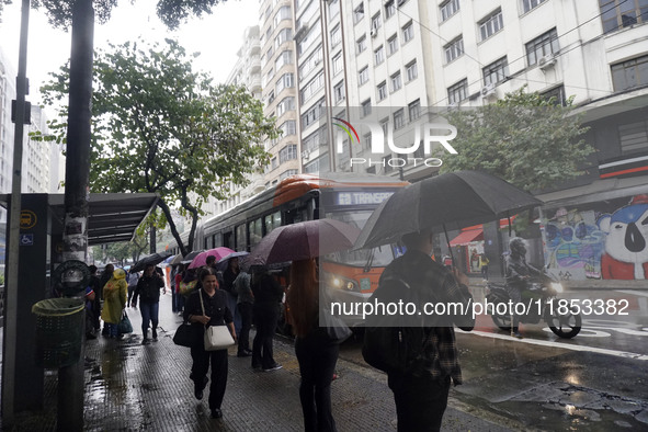 People walk with their umbrellas on a cloudy and rainy day in the center of Sao Paulo, Brazil, on December 10, 2024. 