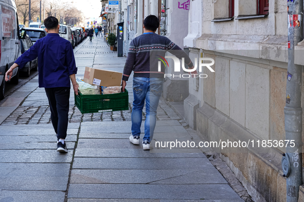 Two Asian men, employees of an Asian snack bar, carry a green crate filled with food and supplies in Dresden, Saxony, Germany, on March 23,...