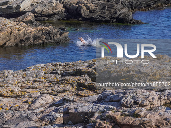 A man takes a dip in the cold waters of the Baltic Sea, jumping from the rocky coast in Gudhjem, Bornholm Island, Denmark, on August 6, 2024...