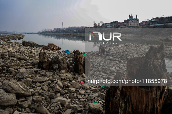 A woman washes utensils near a small water channel formed in the middle of the river Jhelum in Sopore, Jammu and Kashmir, India, on December...