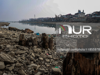 A woman washes utensils near a small water channel formed in the middle of the river Jhelum in Sopore, Jammu and Kashmir, India, on December...