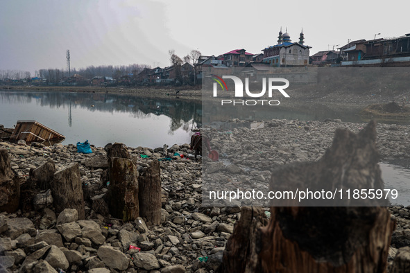 A woman washes utensils near a small water channel formed in the middle of the river Jhelum in Sopore, Jammu and Kashmir, India, on December...