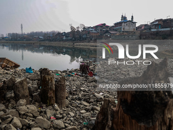 A woman washes utensils near a small water channel formed in the middle of the river Jhelum in Sopore, Jammu and Kashmir, India, on December...