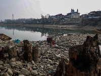 A woman washes utensils near a small water channel formed in the middle of the river Jhelum in Sopore, Jammu and Kashmir, India, on December...