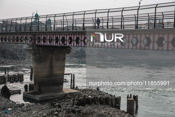 A man walks on a bridge fenced to prevent suicides while another person catches fish in the River Jhelum in Sopore, Jammu and Kashmir, India...