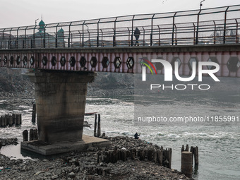 A man walks on a bridge fenced to prevent suicides while another person catches fish in the River Jhelum in Sopore, Jammu and Kashmir, India...