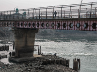 A man walks on a bridge fenced to prevent suicides while another person catches fish in the River Jhelum in Sopore, Jammu and Kashmir, India...