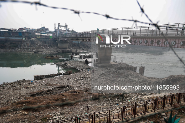 People walk over a bridge as the water level of the Jhelum is lowered due to less rainfall in Sopore, Jammu and Kashmir, India, on December...