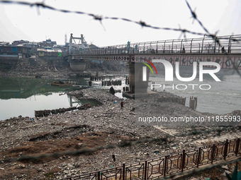 People walk over a bridge as the water level of the Jhelum is lowered due to less rainfall in Sopore, Jammu and Kashmir, India, on December...