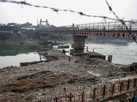 People walk over a bridge as the water level of the Jhelum is lowered due to less rainfall in Sopore, Jammu and Kashmir, India, on December...