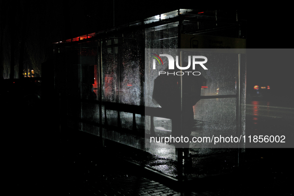 A person with an umbrella stands at a bus stop on Entuziastiv Street in the Rusanivka neighborhood during a power cut in Kyiv, Ukraine, on D...