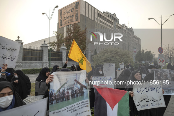 A small group of veiled Iranian women holds a flag of Lebanon's Hezbollah, a Palestinian flag, and placards while participating in a rally t...