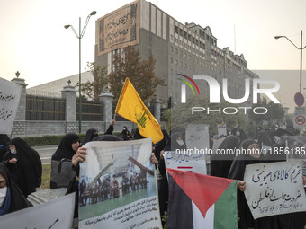 A small group of veiled Iranian women holds a flag of Lebanon's Hezbollah, a Palestinian flag, and placards while participating in a rally t...